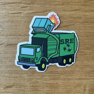 A garbage truck labeled SRE empties a dumpster on fire.